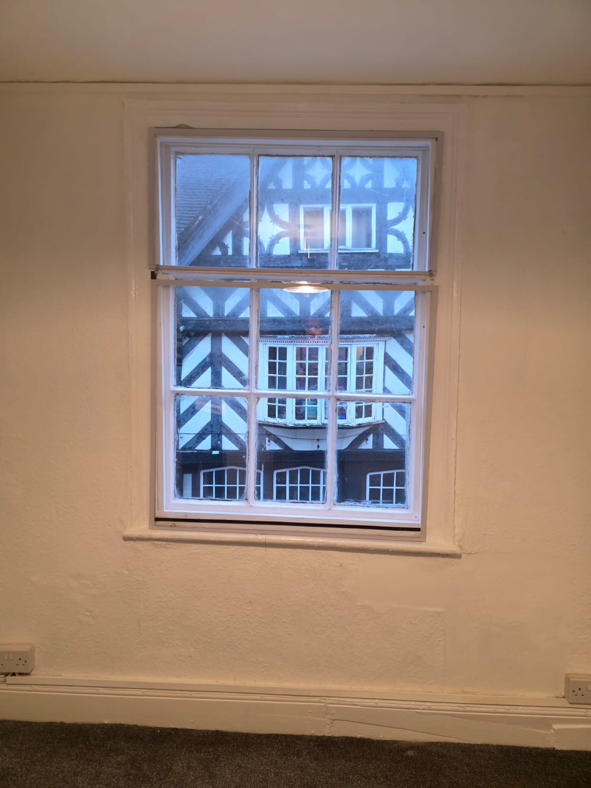 White secondary glazing on sash window in period commercial property overlooking timber-framed buildings
