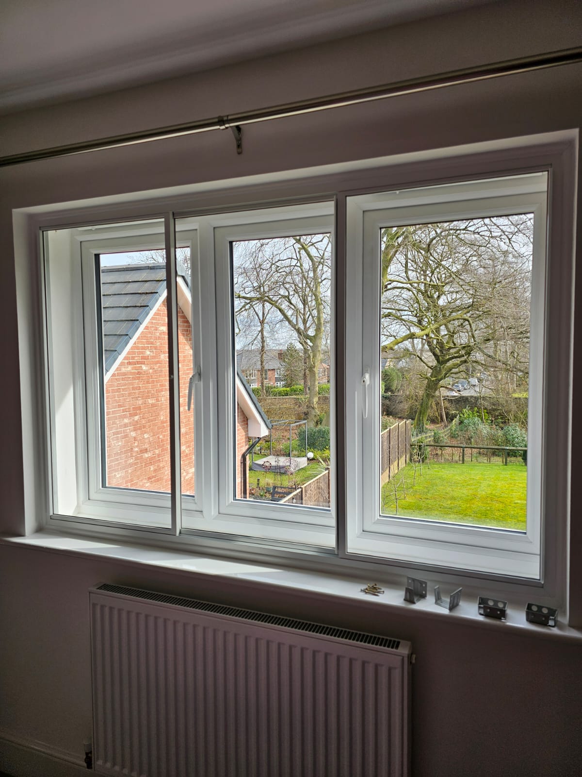 Three-panel hinged secondary glazing on wide residential window with garden views