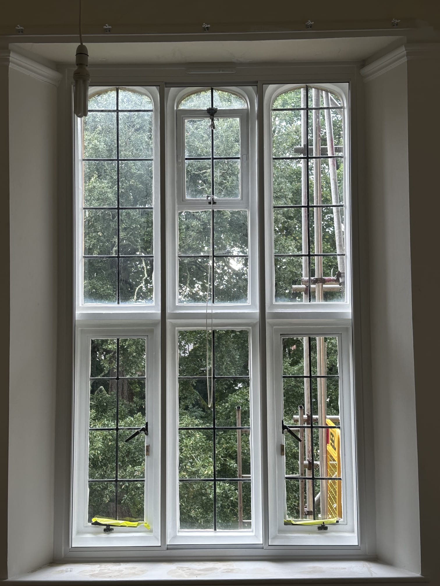 Large three-panel arched secondary glazing on tall heritage property window with tree canopy views
