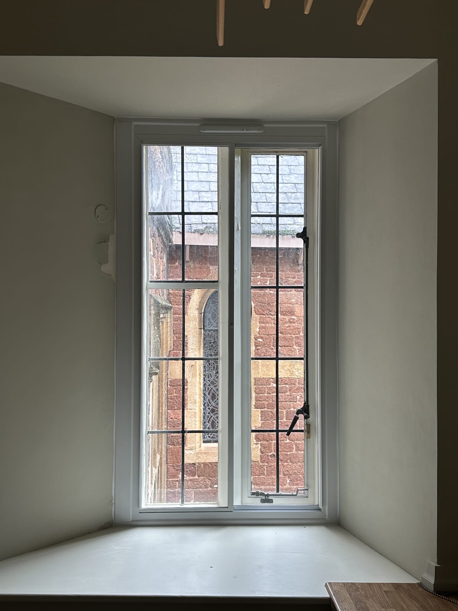 Slim white secondary glazing on double casement window with views of a stone church and garden