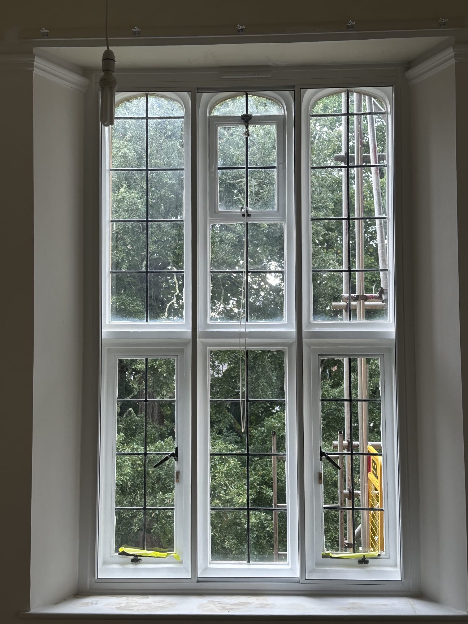 Double arched secondary glazing panels on period property with garden views — white aluminium frame
