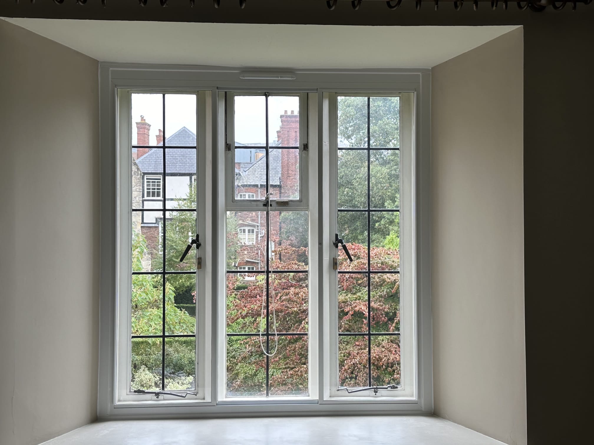 Gothic-arched single-pane secondary glazing on tall narrow heritage window — white aluminium with garden view