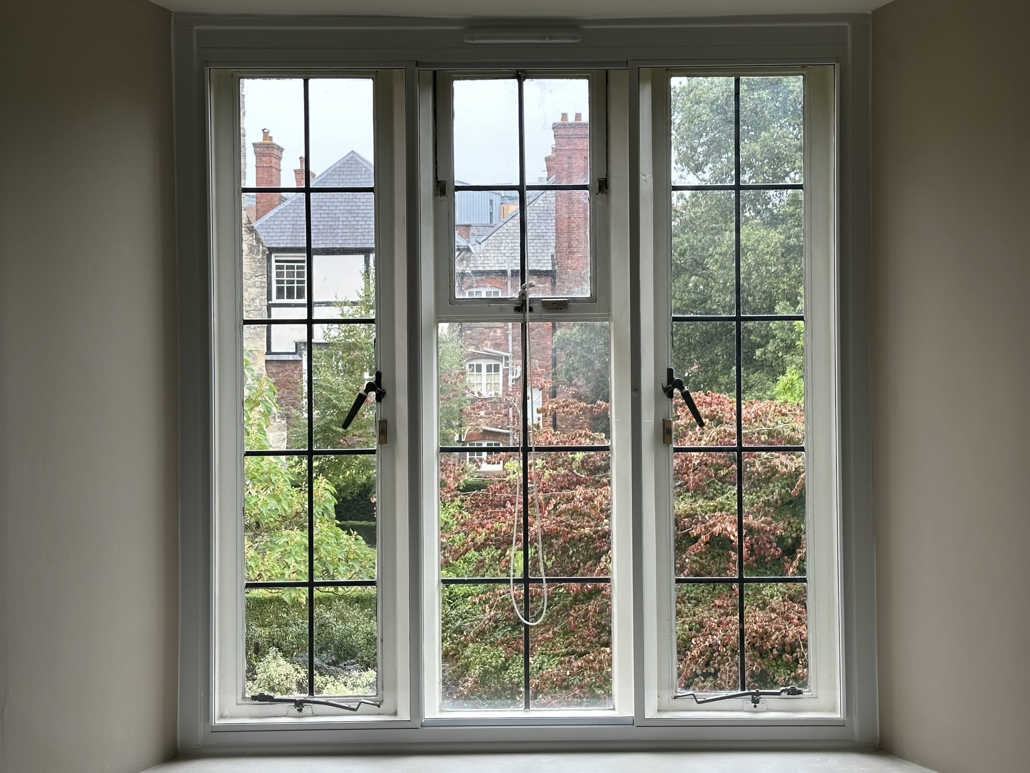 Three-panel white secondary glazing on period property window overlooking Victorian terrace with autumn foliage