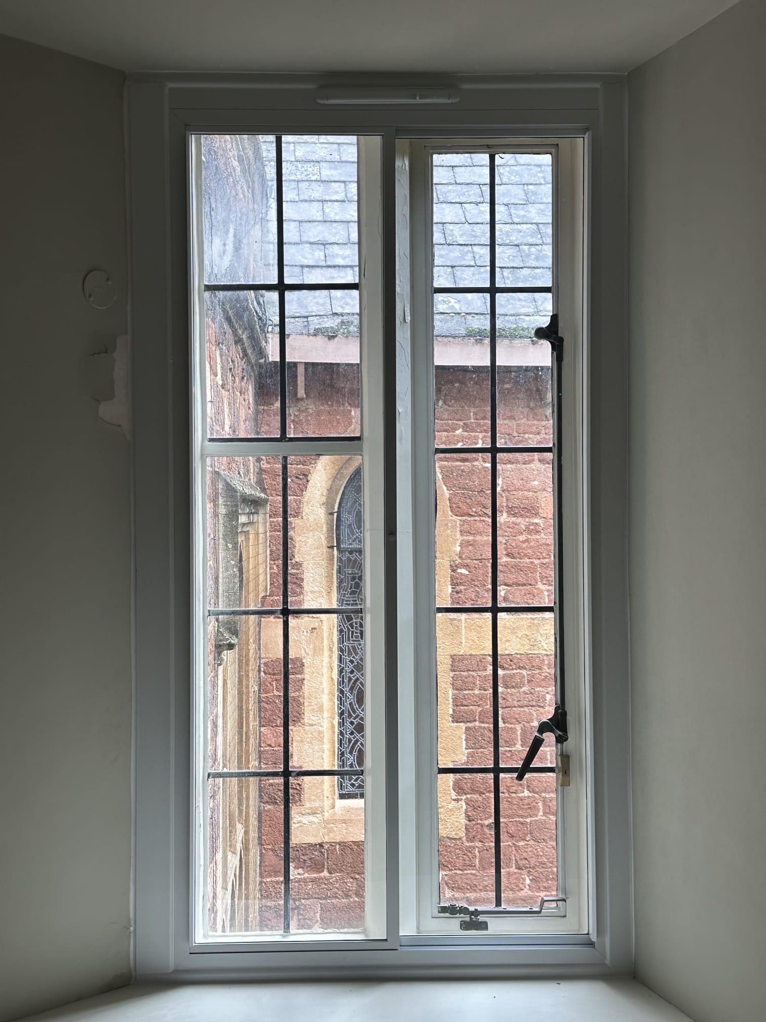 Slim aluminium hinged secondary glazing fitted to casement windows overlooking a stone church