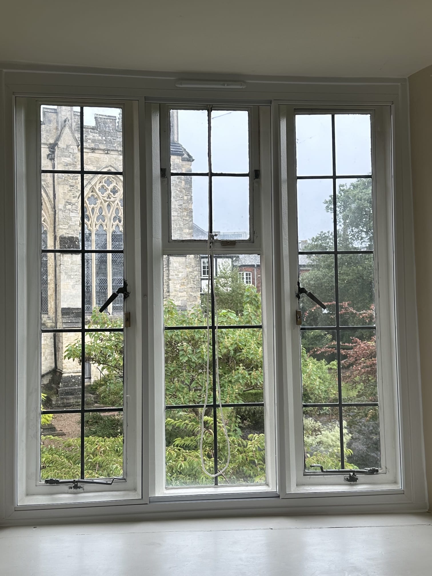 Three-panel vertical sliding secondary glazing on wide heritage windows overlooking churchyard gardens