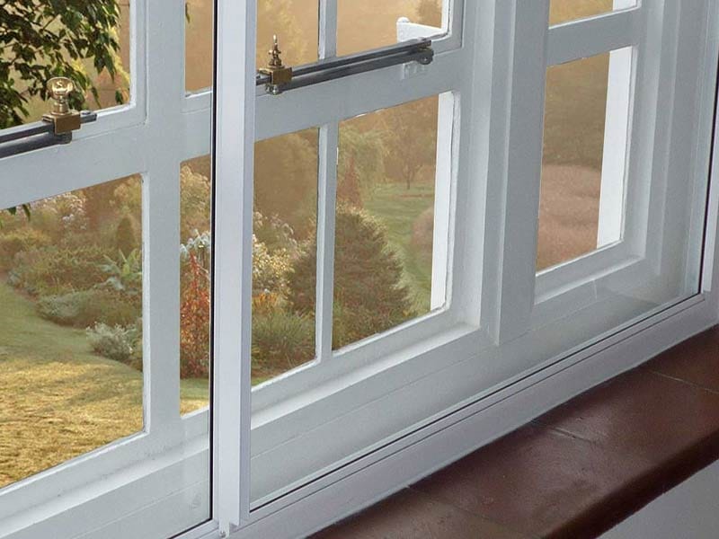 Secondary glazing close-up showing slim aluminium profile and brass hardware on traditional wooden sash window